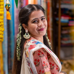 Woman in a floral saree standing in a room with books and decorative items.