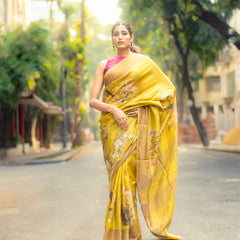 Woman in a yellow saree walking on a street with trees and buildings in the background