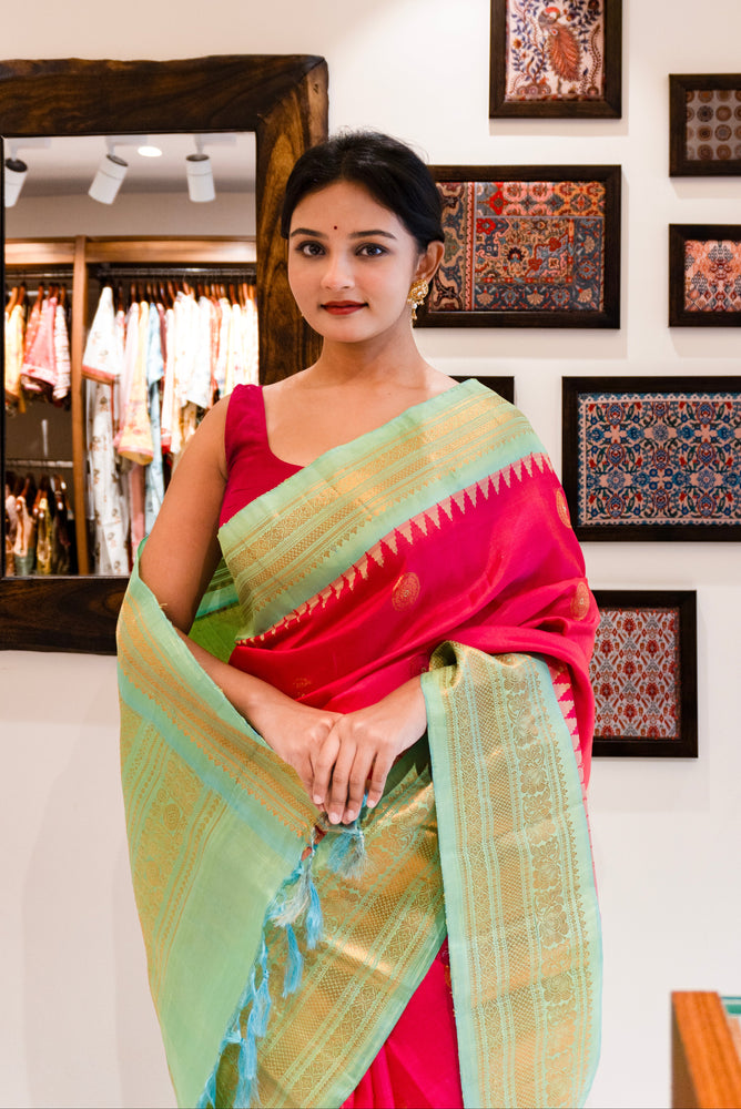 Woman in a pink saree standing in a store with framed artworks on the wall.