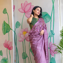 Woman in a purple saree standing in front of a wall with lotus flower designs.