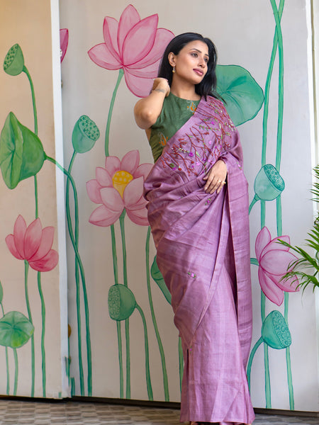 Woman in a purple saree standing in front of a wall with lotus flower designs.