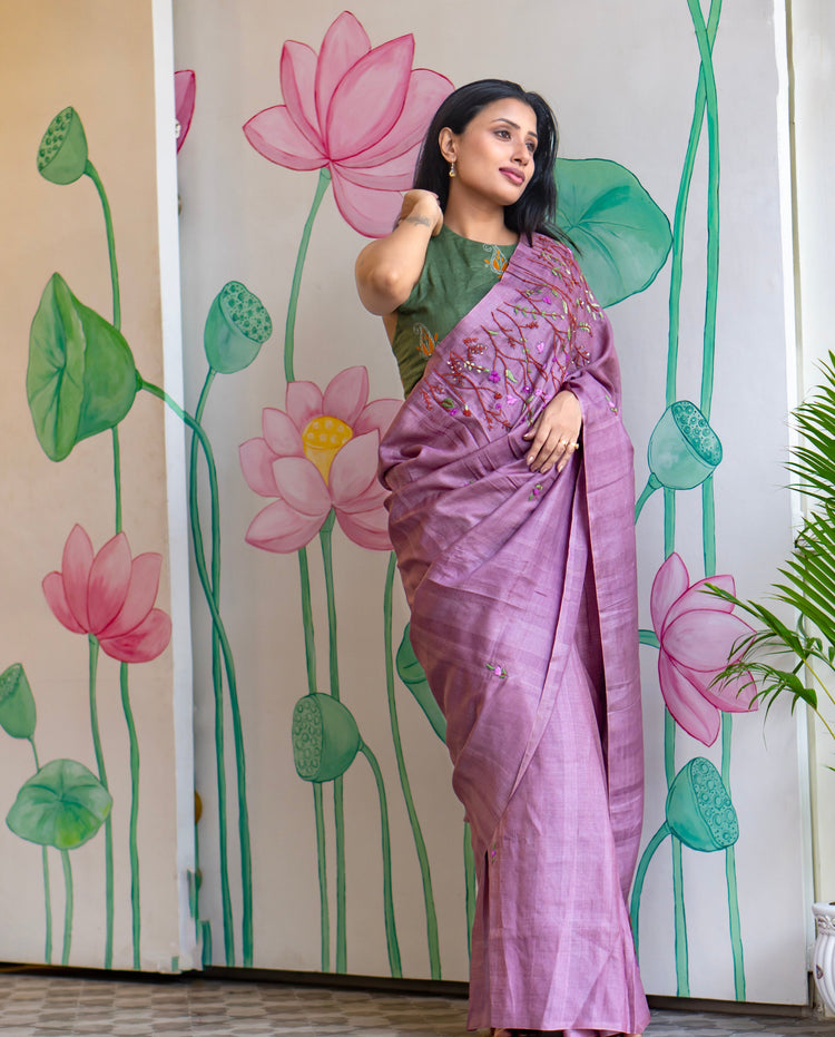 Woman in a purple saree standing in front of a wall with lotus flower designs.