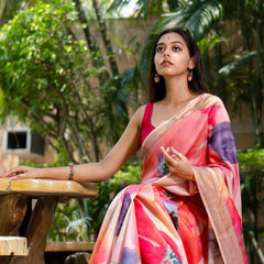 Woman in a colorful saree sitting outdoors with greenery in the background