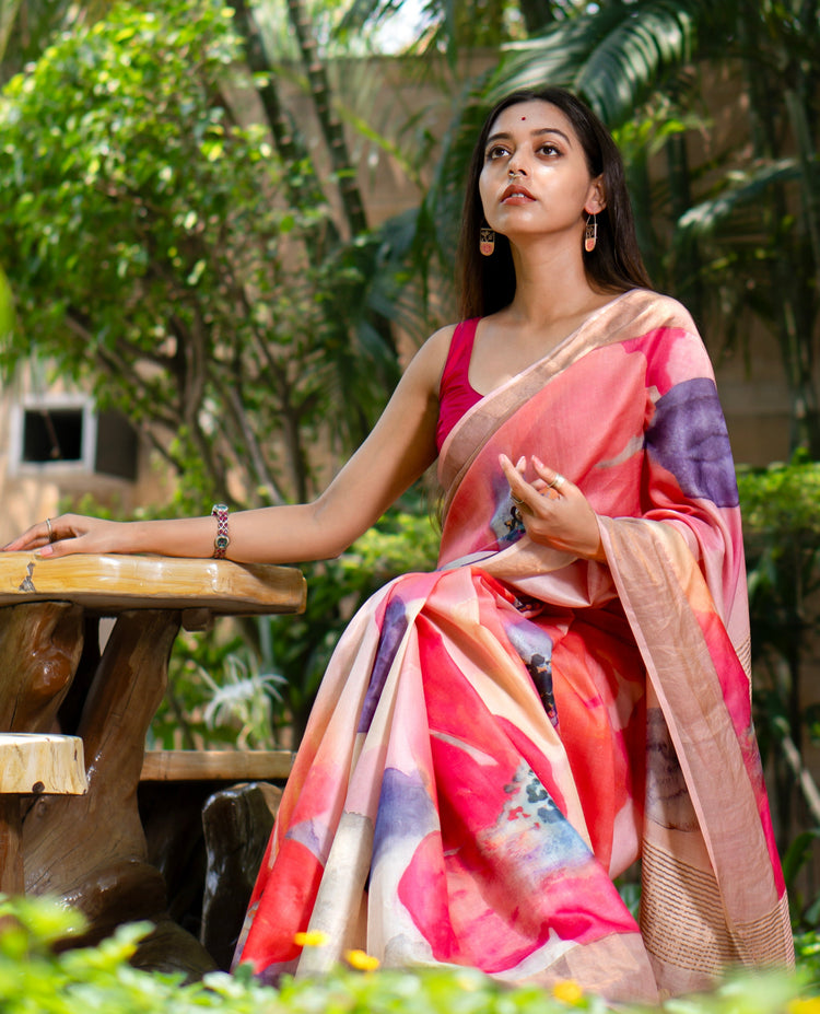 Woman in a colorful saree sitting outdoors with greenery in the background