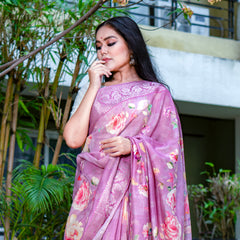Woman wearing a pink floral saree outdoors with greenery in the background