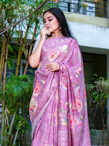 Woman wearing a pink floral saree outdoors with greenery in the background