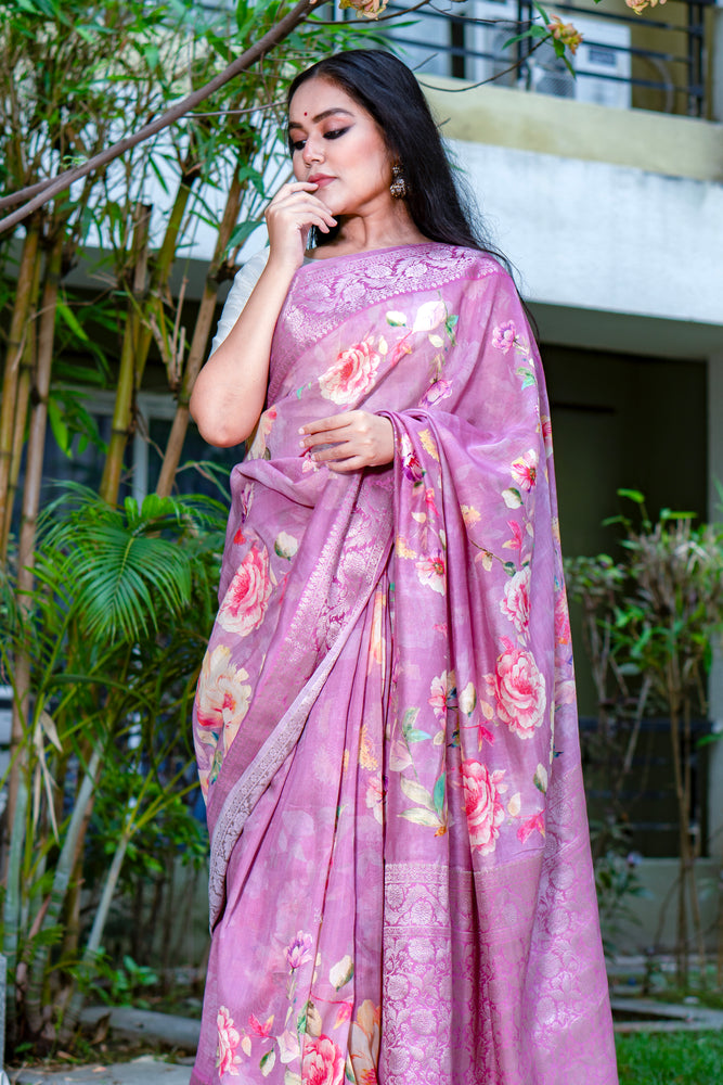 Woman wearing a pink floral saree outdoors with greenery in the background