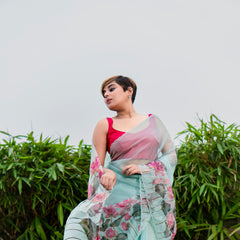 Woman wearing a floral saree with a pink blouse against a green foliage background
